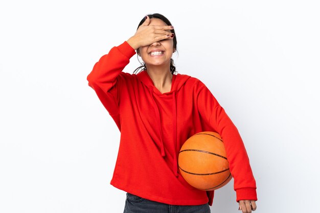 Mulher jovem jogando basquete sobre um branco isolado cobrindo os olhos pelas mãos e sorrindo