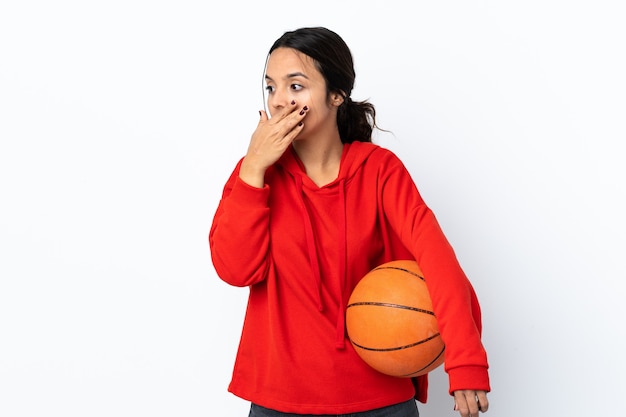 Mulher jovem jogando basquete sobre um fundo branco isolado, cobrindo a boca e olhando para o lado