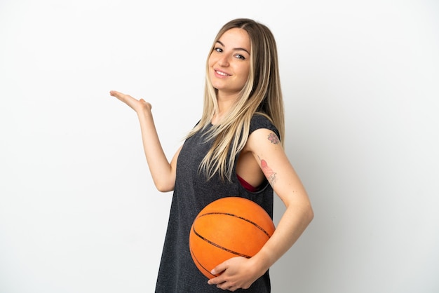 Mulher jovem jogando basquete sobre uma parede branca isolada estendendo as mãos para o lado para convidar para vir