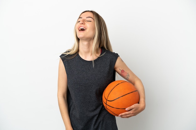 Mulher jovem jogando basquete sobre uma parede branca isolada rindo