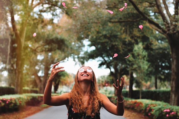 Foto mulher jovem jogando pétala no ar enquanto está de pé no parque