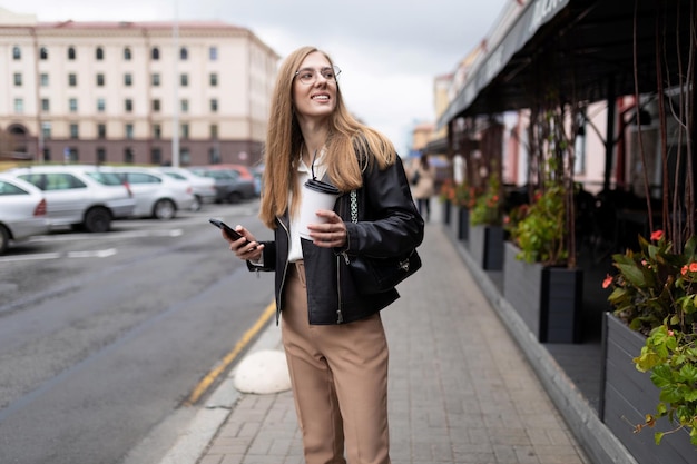 Mulher jovem jornalista caminha pela cidade com café nas mãos