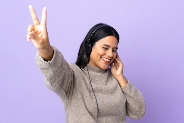 Mulher jovem latina na parede roxa, ouvir música e cantar