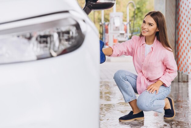 Mulher jovem lavando carro com pano azul na estação de autoatendimento