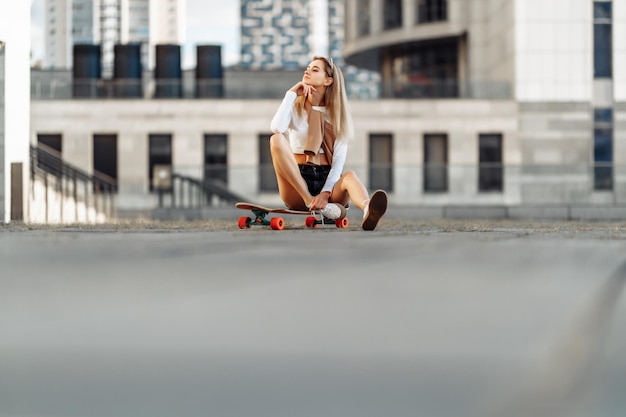 Mulher jovem legal com uma prancha sentada nas escadas com óculos de sol estilo casual de alta qualidade