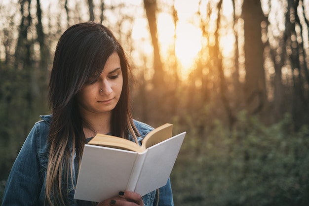 Foto mulher jovem lendo um livro com árvores ao fundo