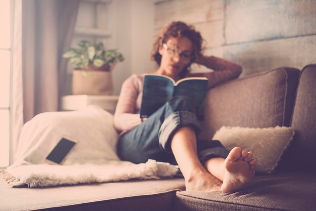 Foto mulher jovem lendo um livro enquanto se relaxa no sofá em casa