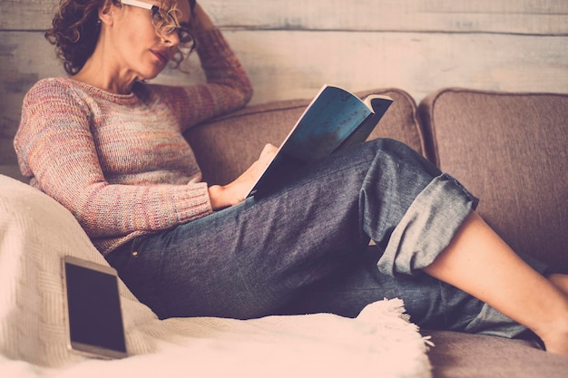 Mulher jovem lendo um livro enquanto se relaxa no sofá em casa