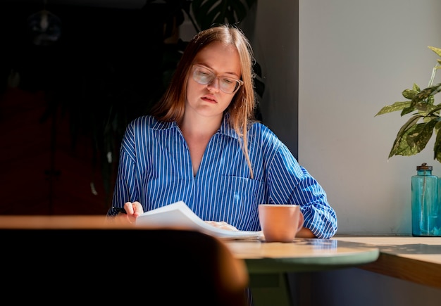 Mulher jovem lendo um livro ou programa de estudos sentada na mesa de um café com uma xícara de café