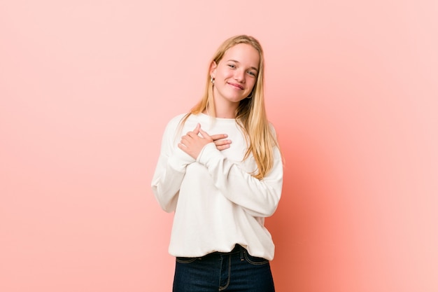 Mulher jovem loira adolescente tem expressão amigável, pressionando a palma da mão no peito. Conceito de amor