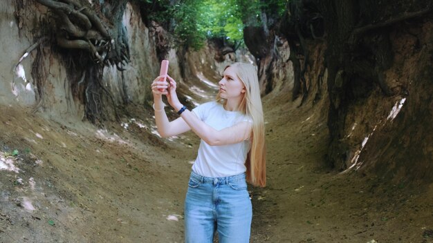 Mulher jovem loira fazendo fotos em um smartphone no mágico Roots Gorge, situado em Kazimierz Dolny, na Polônia