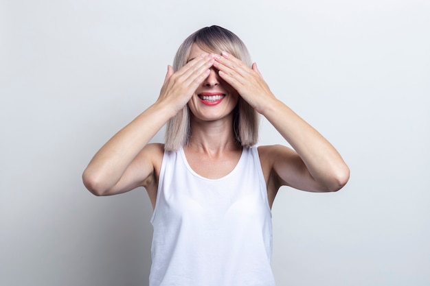 Mulher jovem loira sorridente com as palmas das mãos fechou os olhos sobre um fundo claro.