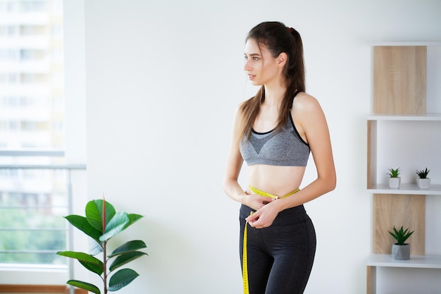 Mulher jovem magro, medindo sua cintura fina com uma fita métrica