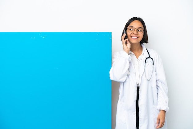 Mulher jovem médica de raça mista com um grande cartaz isolado no fundo branco, conversando com o celular