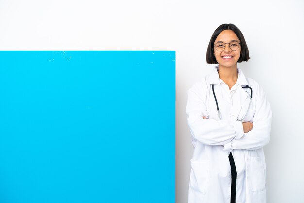 Mulher jovem médica mestiça com um grande cartaz isolado no fundo branco mantendo os braços cruzados na posição frontal