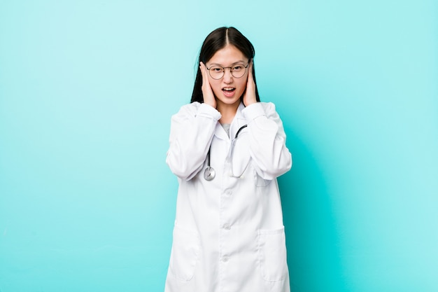 Mulher jovem médico chinês cobrindo os ouvidos com as mãos, tentando não ouvir som muito alto.