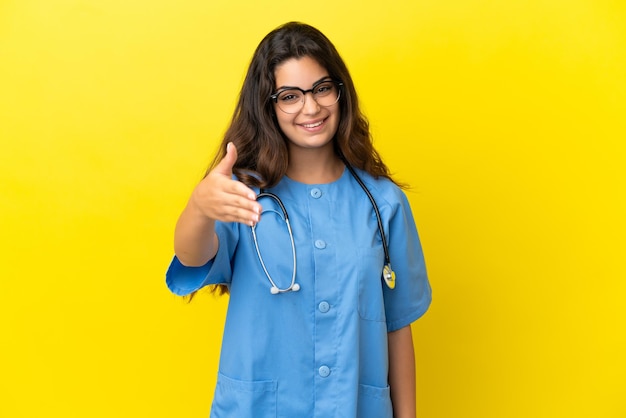Mulher jovem médico cirurgião isolada em fundo amarelo apertando as mãos para fechar um bom negócio