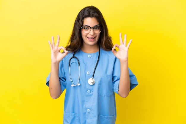 Mulher jovem médico cirurgião isolada em fundo amarelo mostrando sinal de ok com os dedos