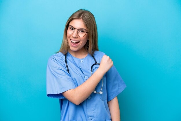 Mulher jovem médico cirurgião isolada em fundo azul comemorando uma vitória