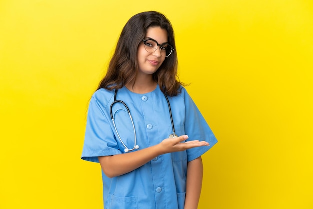 Mulher jovem médico cirurgião isolada em um fundo amarelo apresentando uma ideia enquanto olha sorrindo para