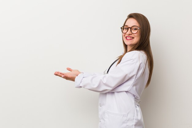 Mulher jovem médico contra uma parede branca, segurando um espaço de cópia em uma palma.