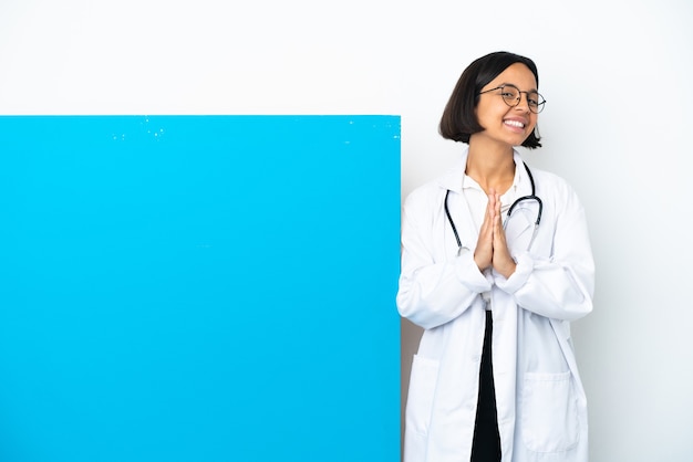 Mulher jovem médico de raça mista com um grande cartaz isolado no fundo branco mantém as palmas das mãos juntas. Pessoa pede algo