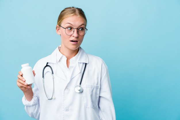 Mulher jovem médico russo segurando o frasco de comprimidos em azul, sendo chocado por causa de algo que ela viu.