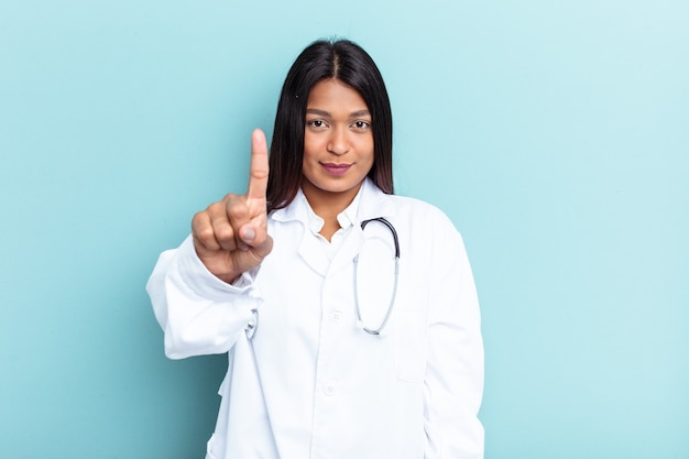 Mulher jovem médico venezuelana isolada sobre fundo azul, mostrando o número um com o dedo.