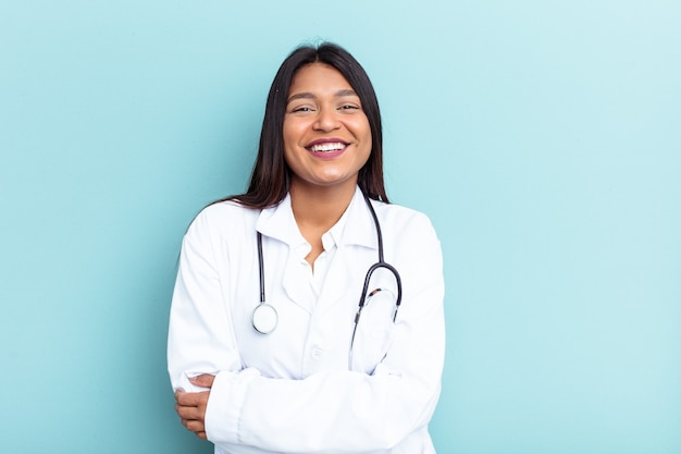 Mulher jovem médico venezuelana isolada sobre fundo azul rindo e se divertindo.