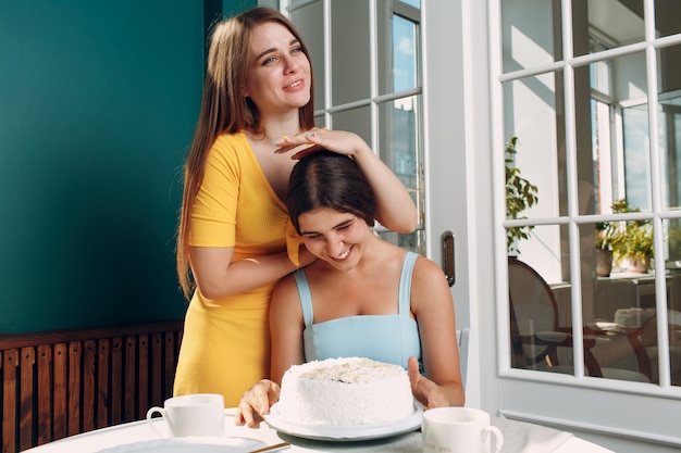 Mulher jovem mergulha o rosto em um bolo branco com creme. Conceito de feliz aniversário.