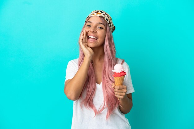 Mulher jovem mestiça com um sorvete de corneta isolado em um fundo azul gritando com a boca bem aberta