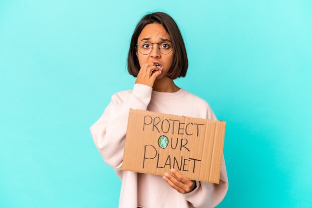 Mulher jovem mestiça hispânica segurando um protetor de papelão do planeta roendo as unhas, nervosa e muito ansiosa.