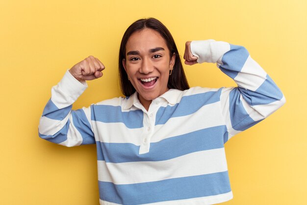 Mulher jovem mestiça isolada em fundo amarelo mostrando gesto de força com os braços, símbolo do poder feminino