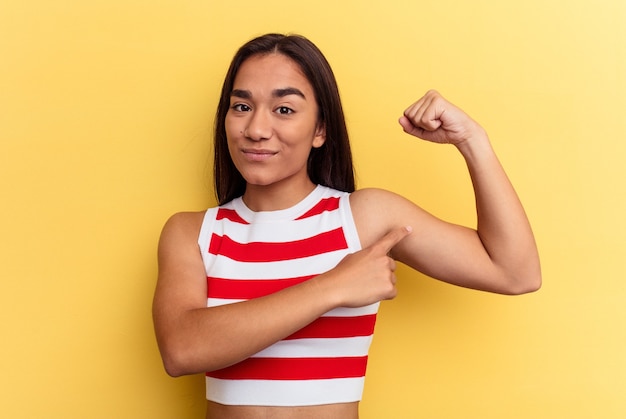 Mulher jovem mestiça isolada em fundo amarelo mostrando gesto de força com os braços, símbolo do poder feminino