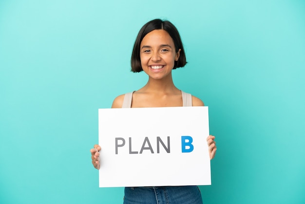 Mulher jovem mestiça isolada em fundo azul segurando um cartaz com a mensagem PLANO B com expressão feliz