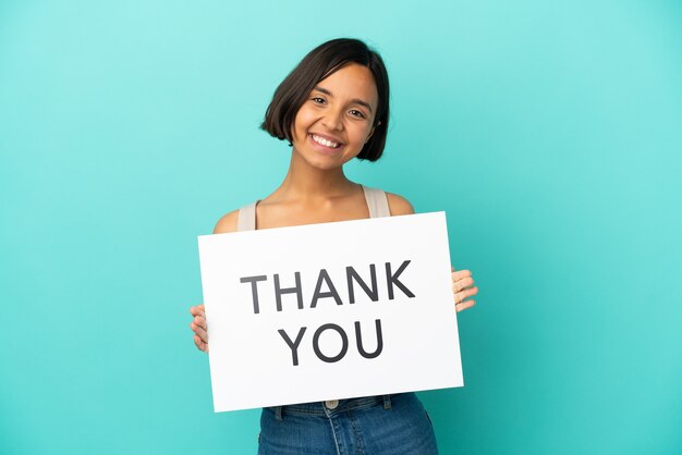 Mulher jovem mestiça isolada em fundo azul segurando um cartaz com o texto OBRIGADO com expressão feliz