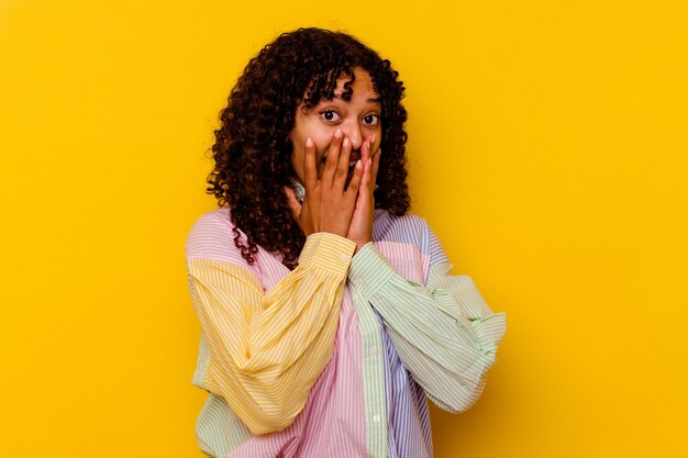 Mulher jovem mestiça isolada em um fundo amarelo chocada, cobrindo a boca com as mãos, ansiosa para descobrir algo novo.