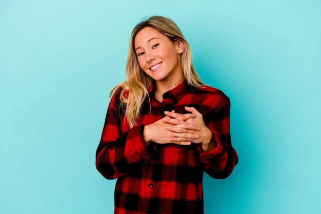 Mulher jovem mestiça isolada na parede azul tem uma expressão amigável, pressionando a palma da mão no peito. Conceito de amor.