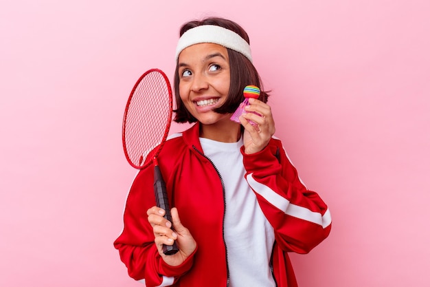 Mulher jovem mestiça jogando badminton isolada na parede rosa