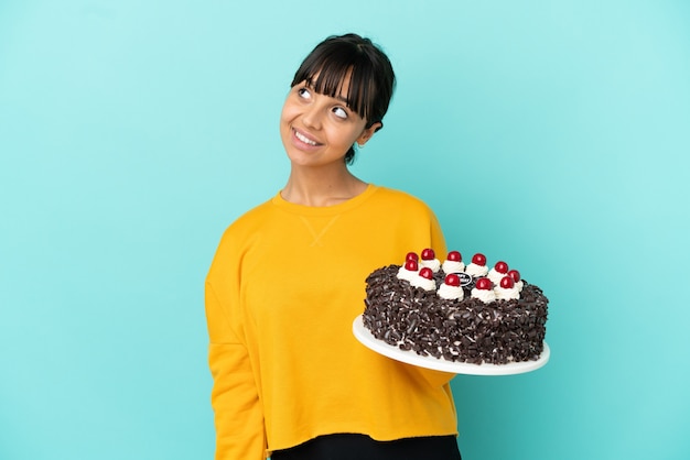 Mulher jovem mestiça segurando bolo de aniversário olhando para cima enquanto sorri