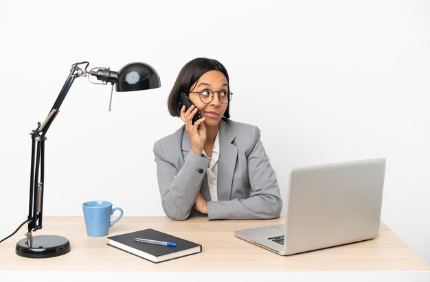 Mulher jovem, mestiça, trabalhando no escritório, conversando com alguém ao telefone celular