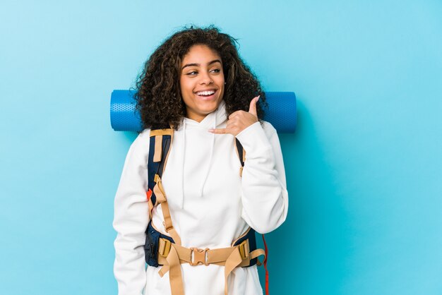 Mulher jovem mochileiro americano africano mostrando um gesto de chamada de telefone móvel com os dedos.