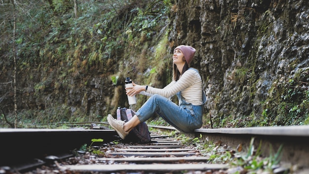 Mulher jovem mochileiro está sentado no trilho do trem e descansando sozinho