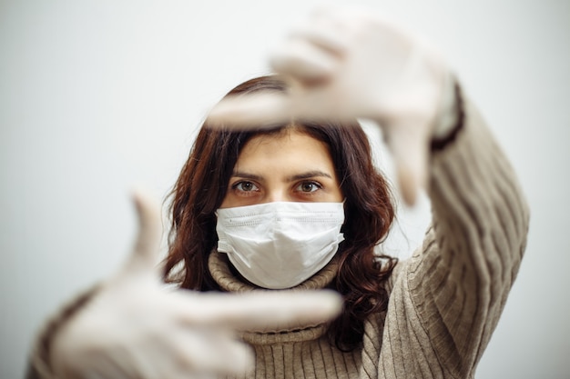 Foto mulher jovem mostra o quadro com as mãos e precisa ficar em casa durante a quarentena devido à pandemia de coronavírus. linda garota usando luvas e máscara médica. conceito de epidemia de covid-19.