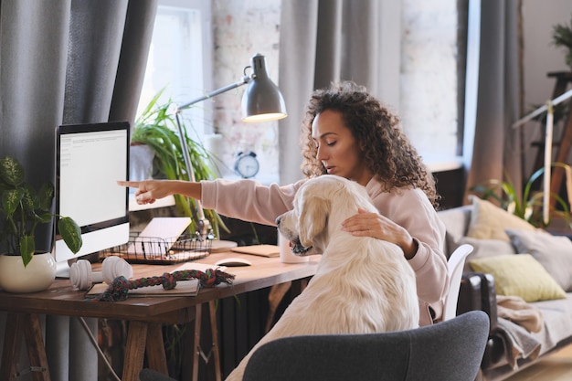 Foto mulher jovem mostrando algo para o cachorro no computador durante uma conversa online em casa