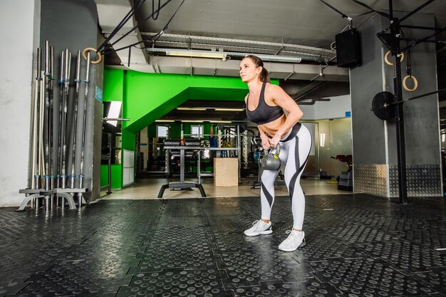 Mulher jovem musculosa realizando exercícios de barra de levantamento morto em estúdio