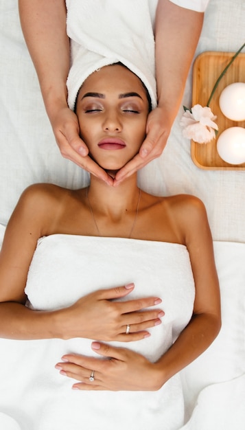 Mulher jovem na cama de exame ou na mesa de massagem, recebendo um procedimento facial cosmético rejuvenescedor para uma pele fresca e perfeita, feito por um profissional de cuidados com a pele no salão de beleza ou sala de spa. Vista superior