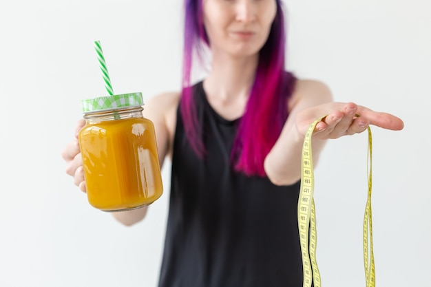 Mulher jovem não identificada segurando um suco de proteína frutado com um canudo e fita métrica