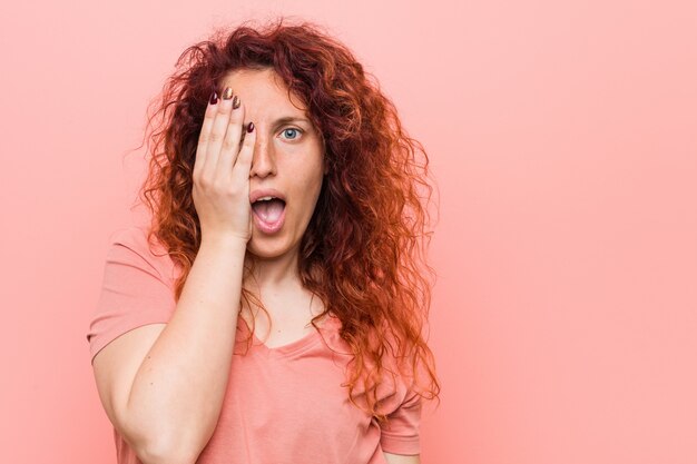 Mulher jovem natural e autêntica ruiva se divertindo cobrindo metade do rosto com a palma da mão.