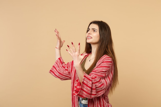 Mulher jovem nervosa perplexa em roupas casuais, olhando de lado, levantando-se espalhando as mãos isoladas no fundo da parede bege pastel no estúdio. Emoções sinceras de pessoas, conceito de estilo de vida. Simule o espaço da cópia.